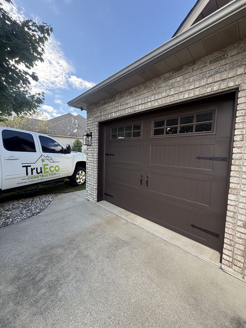 Dark brown carriage-style garage door with top windows on a brick garage