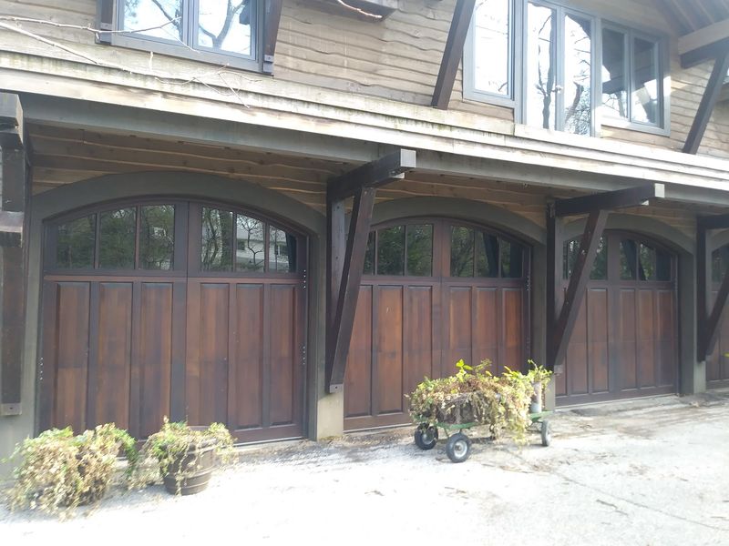Three stained-wood carriage-style garage doors with arched tops and window panels