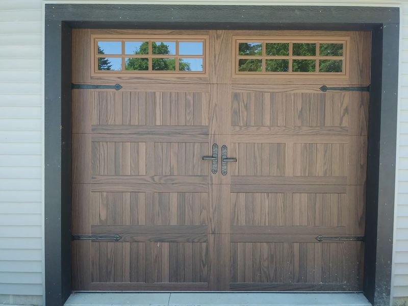 Wide wood-grain carriage garage door with a row of divided-light windows and black hardware