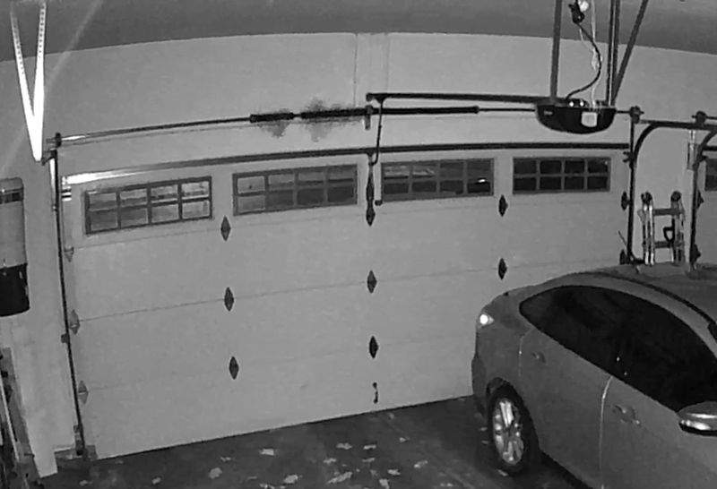 Inside a garage: white raised-panel door with windows, tracks and a garage door opener