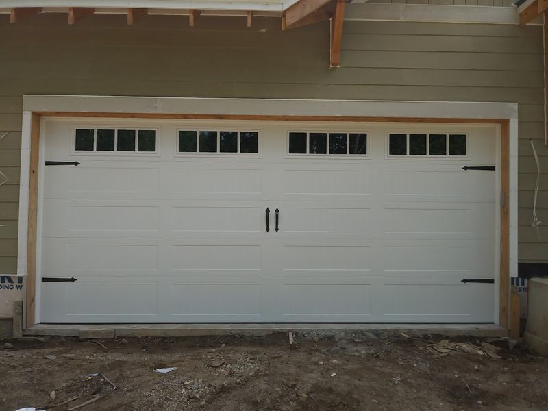 White carriage-house garage door with a top row of windows and black strap hinges on a new build